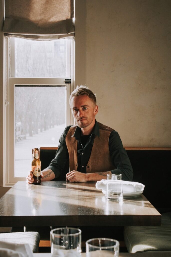 Jay Bowcott in front of a window sitting at a Table with a bottle